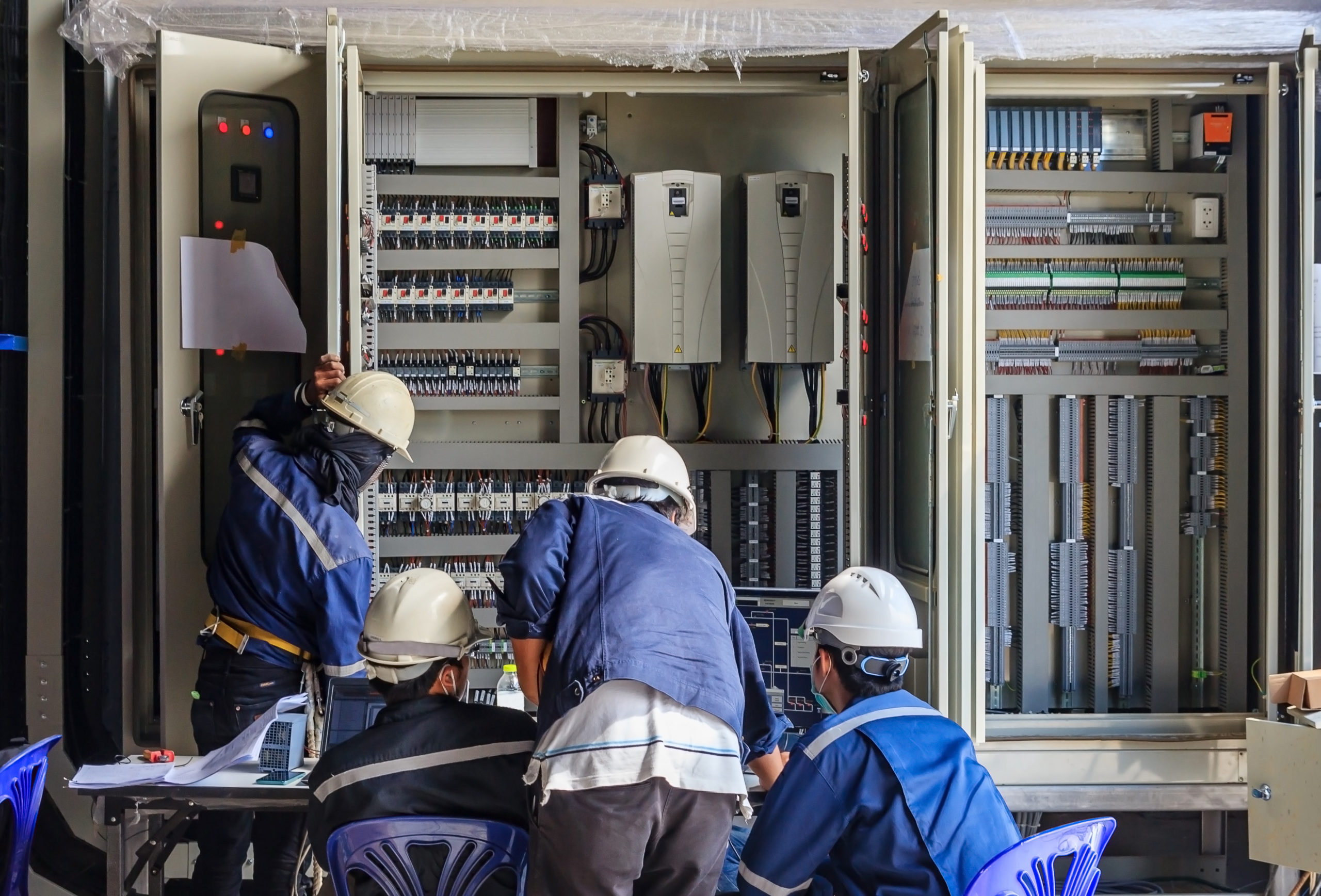 Engineer performing maintenance on wiring and equipment inside a PLC cabinet while monitoring a step-up transformer