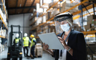 Woman manager with protective shield uisng tablet indoors in warehouse, coronavirus concept.