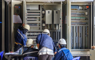 Ingénieur effectuant la maintenance des câblages et équipements dans une armoire PLC tout en surveillant un transformateur élévateur