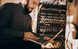 Ingénieur configurant des systèmes industriels depuis un ordinateur entre des panneaux de câblage électrique