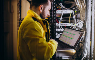 Technicien en équipement de sécurité consultant des indicateurs numériques sur ordinateur devant des armoires électriques industrielles